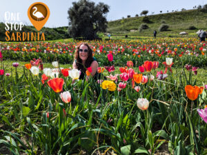 A woman enjoying the vibrant tulips at Giardino dei Tulipani in Turri, Sardinia, wearing sunglasses on a sunny day