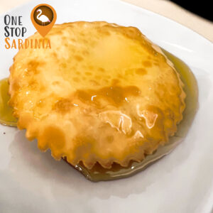 A golden seadas pastry topped with honey on a white plate.