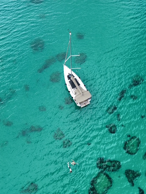 Clear blue green water of mediterranean sea at the coast pf Sardinia with a white boat floating in the center